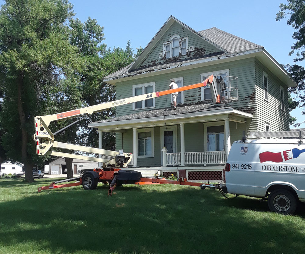 Two-story exterior repaint, worked from a boom lift beside the crew van.