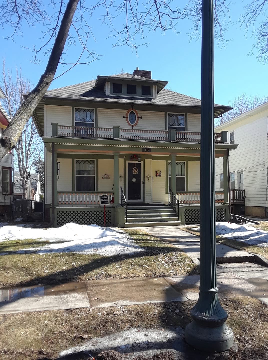 American Foursquare exterior in cream with sage-green trim and accent-striped porch rails, leaded-glass windows, snow patches on the lawn
